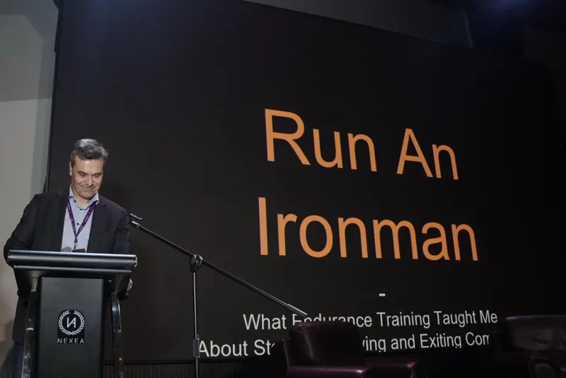 Harald at a NEXEA lectern in front of a slide that reads Run An Ironman